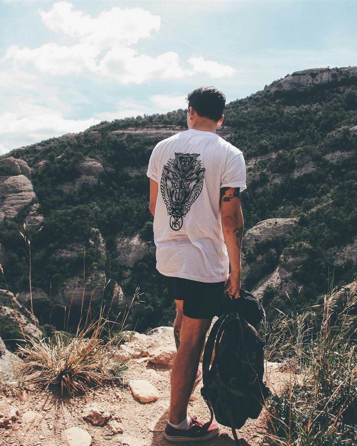 A man walking a hillside path in a white t-shirt